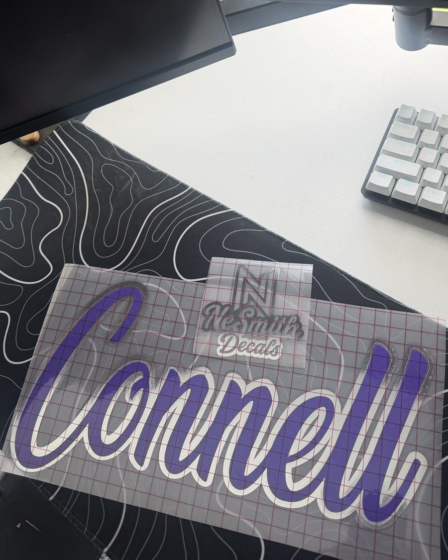 Purple script name decal with a white outline and chrome shadow, on transfer tape